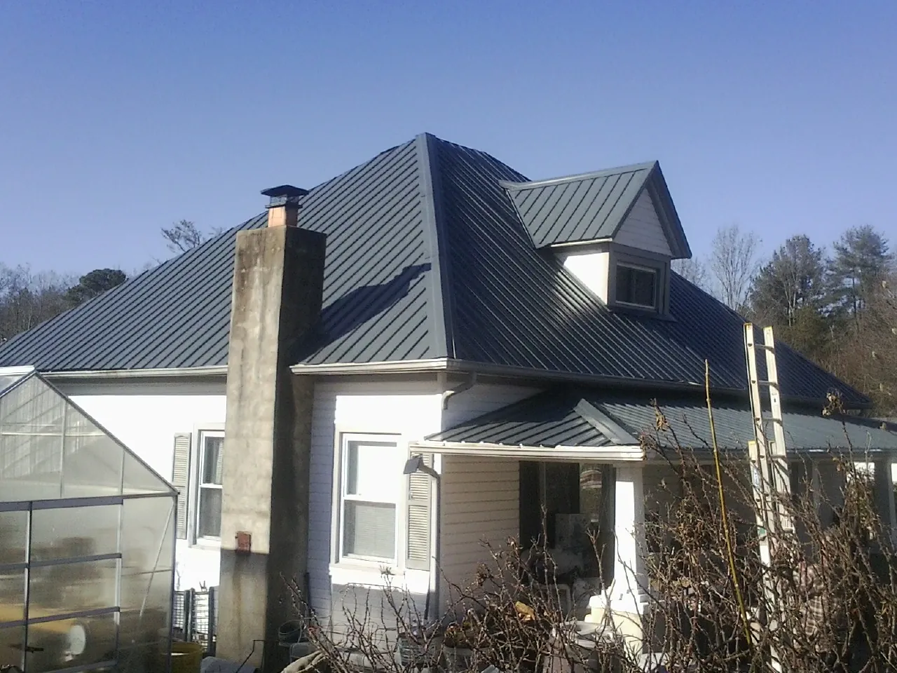 Dark blue standing seam metal roof on a white farmhouse with dormer — Slate & Tile Roof Repair by Roofing Brothers in Preemption