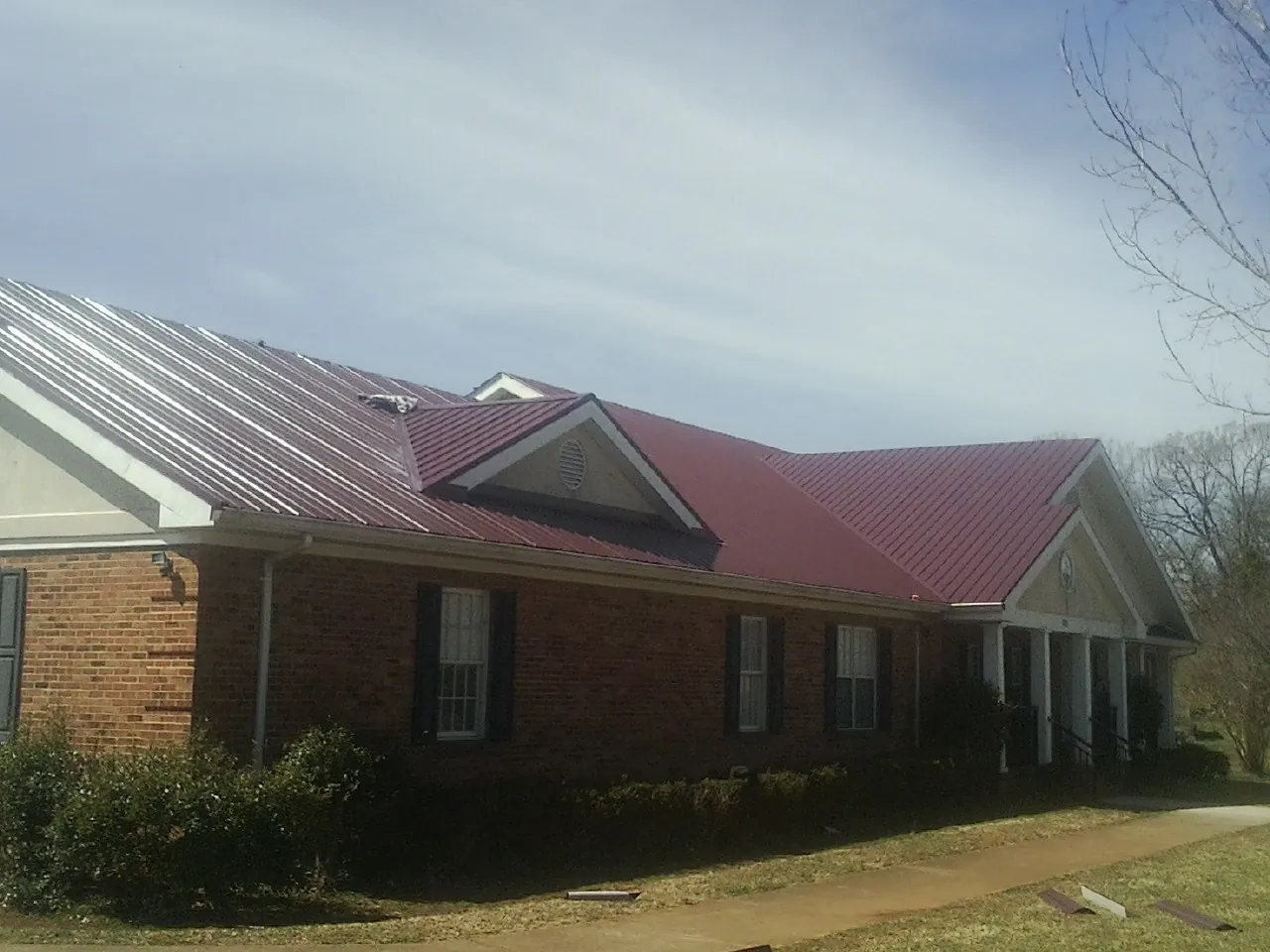 Red metal roof with gabled entries on a long brick building, from a Hail Damage Roof Repair job in Preemption