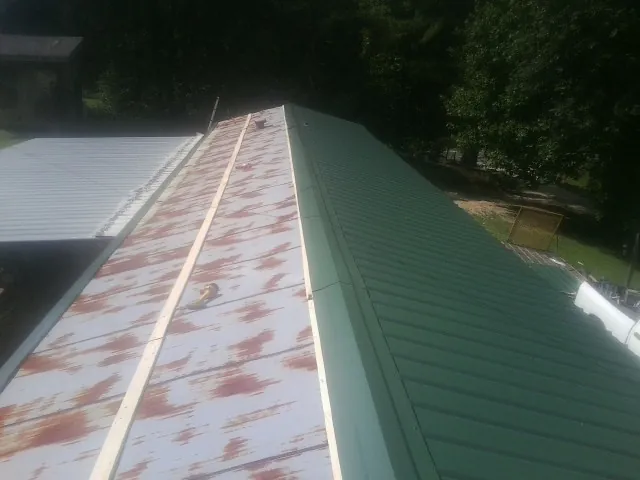 Old rusted panels beside newly installed green metal roofing — Wind Damage Roof Repair by Roofing Brothers in Preemption