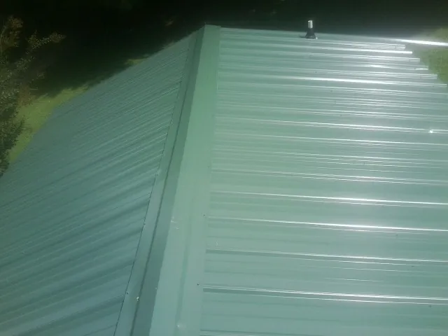 New green metal panels meeting at the ridge of a roof — Flat Roof Repair work by our crew in Preemption