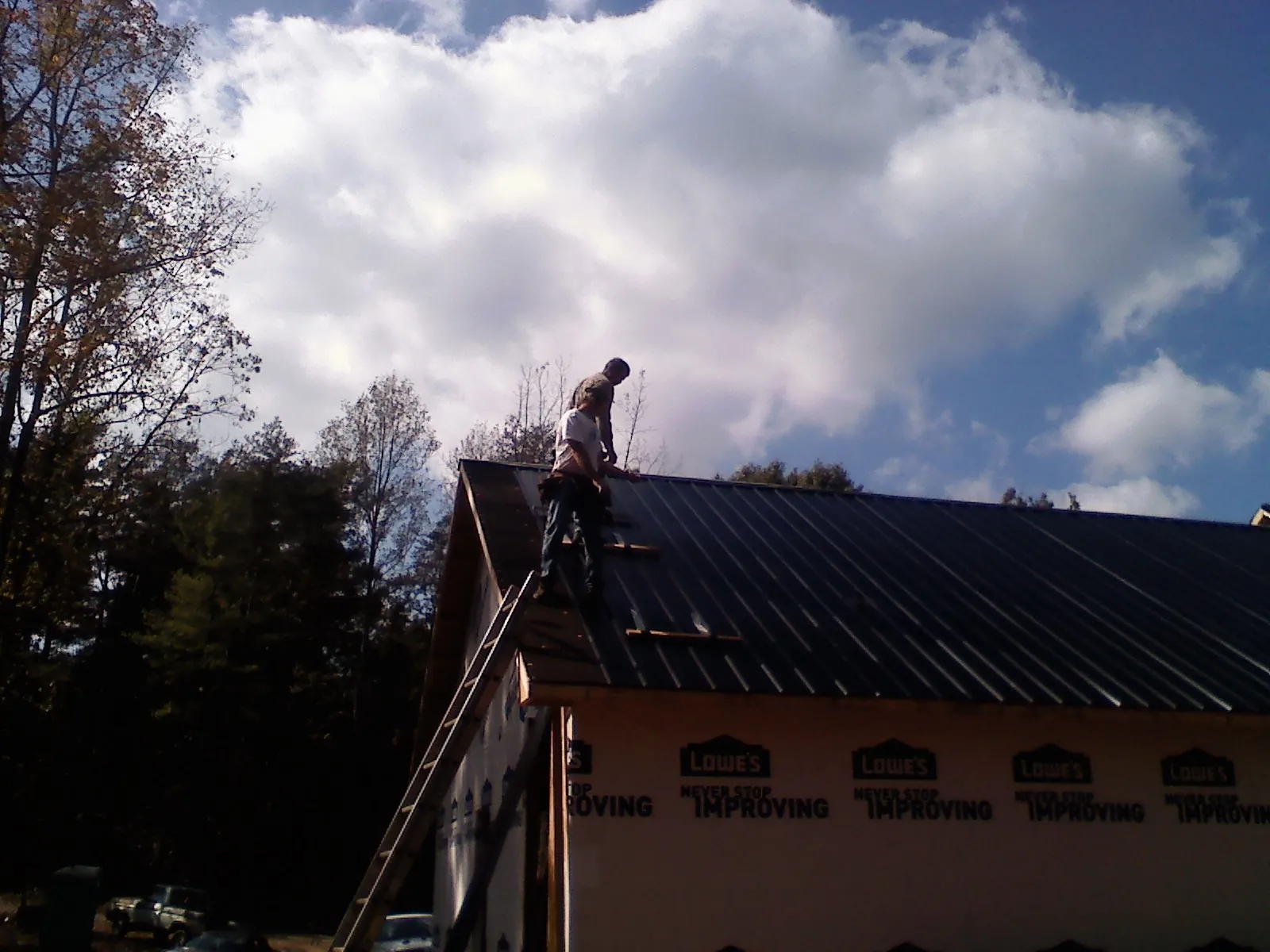 Roofer fastening dark metal panels high against a cloudy sky, from a Roof Inspection job in Preemption
