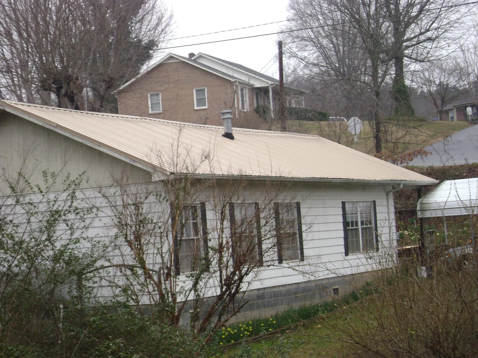 Tan metal roof on a white sided house set into a hillside — Commercial Roofing by Roofing Brothers in Preemption